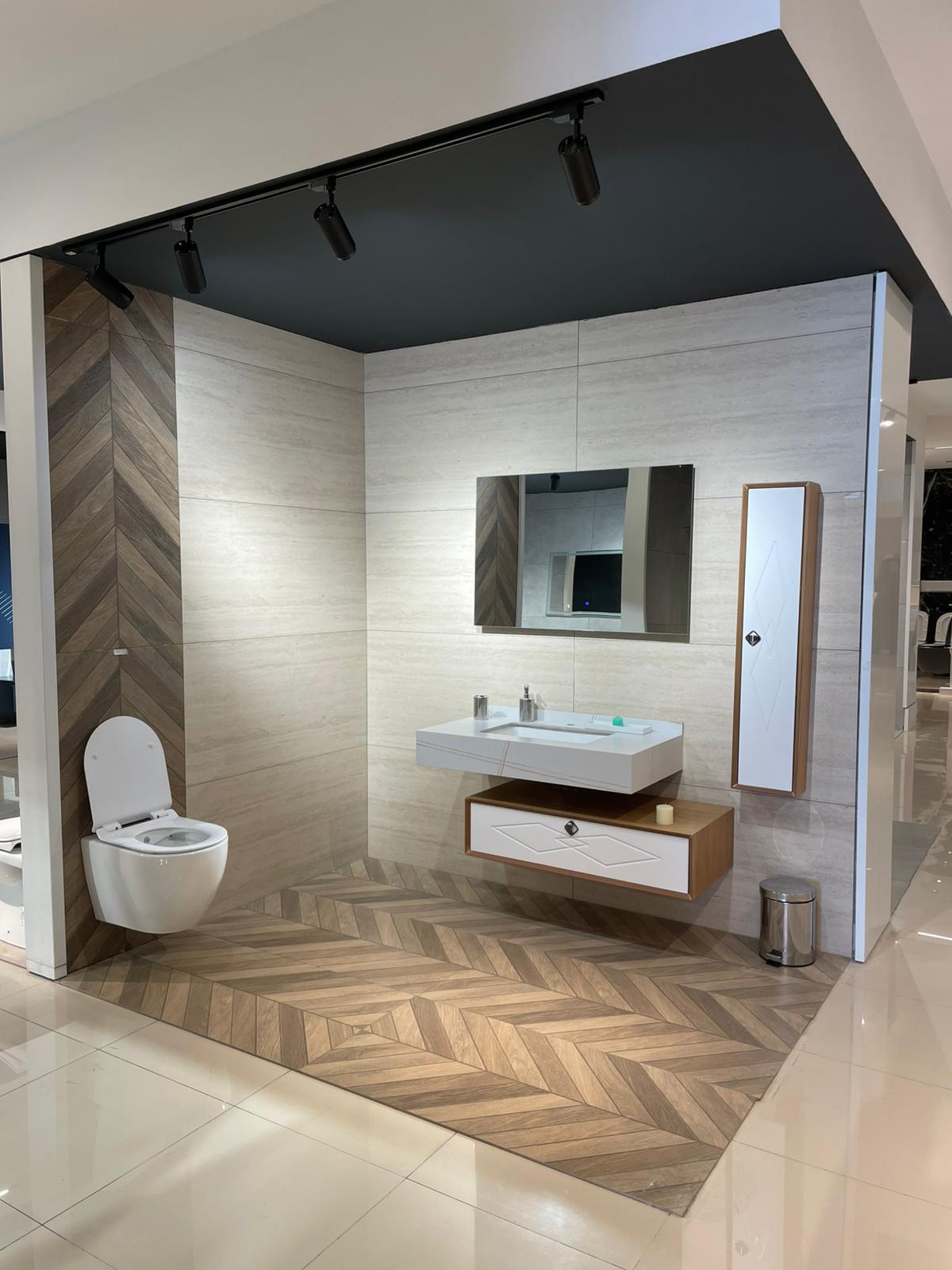 Moderno kupatilo sa elegantnim elementima, uključujući lavabo sa drvenim detaljima, ogledalo i WC školjku. Zidovi su obloženi kombinacijom svetlih i tamnih tonova, što stvara sofisticiran izgled.