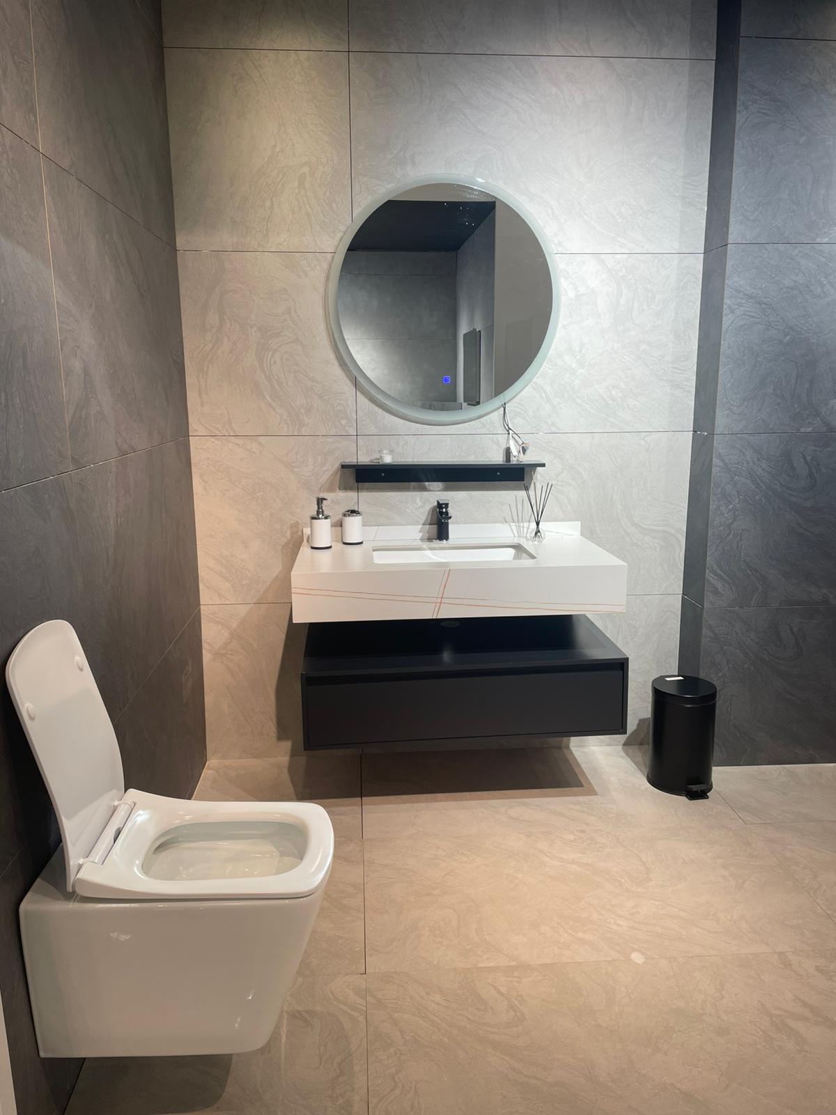 Moderno kupatilo sa minimalističkim dizajnom, uključuje elegantan lavabo sa ogledalom i toalet. Zidovi su obloženi pločicama u neutralnim tonovima, što stvara sofisticiranu atmosferu.