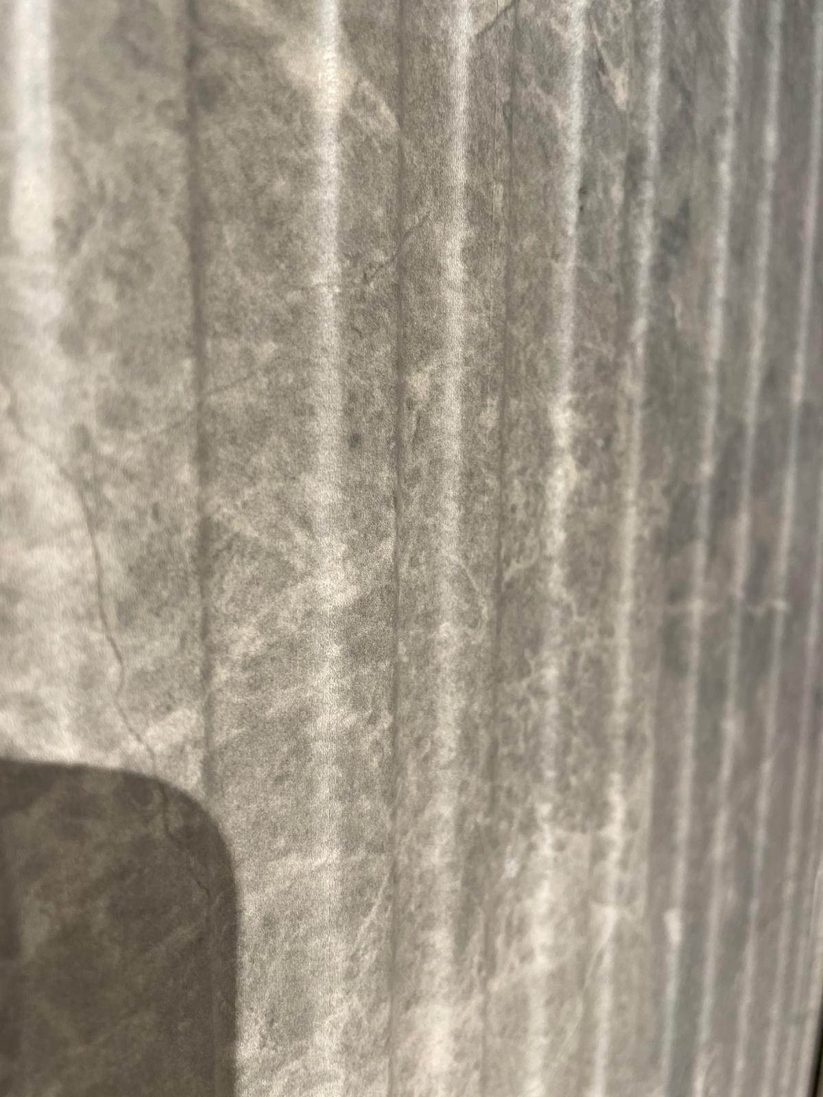 Ova slika prikazuje teksturu materijala koji se koristi u kupatilskoj opremi, sa naglaskom na reljefne linije koje mogu biti deo staklene ili plastične površine.