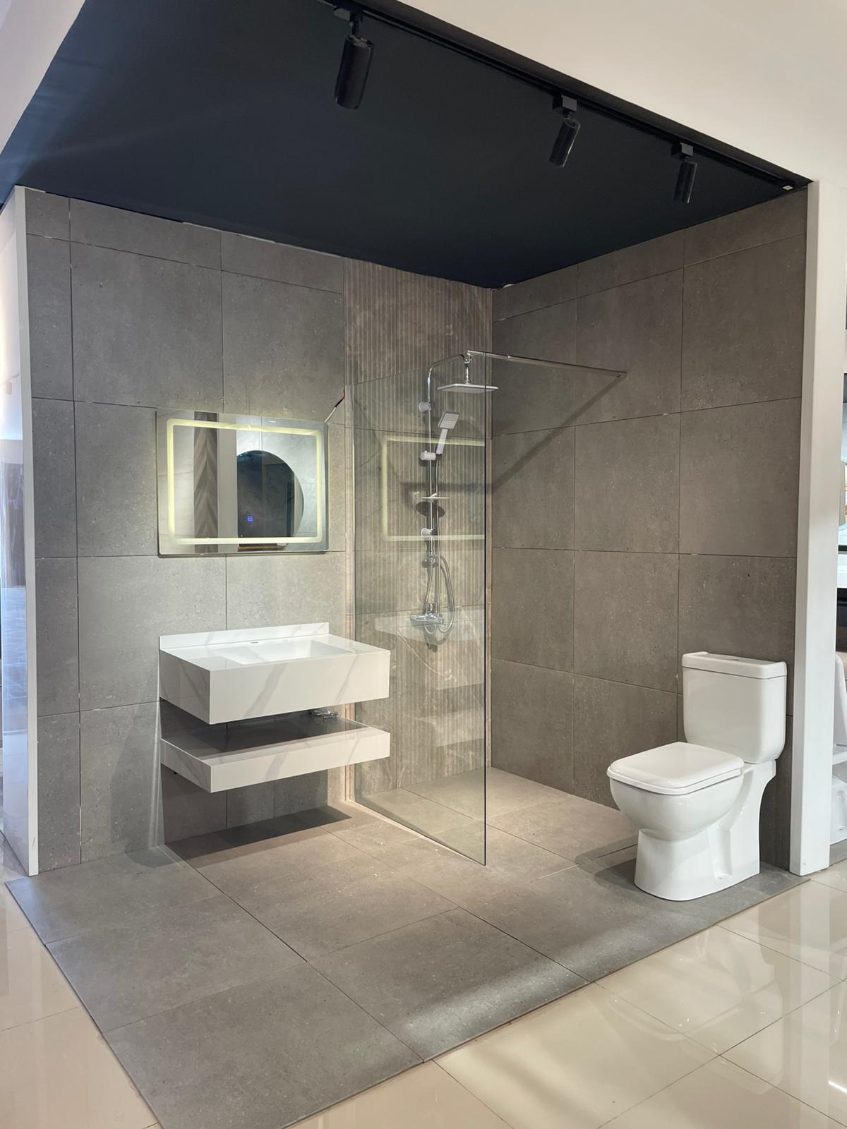 Moderno kupatilo sa elegantnim dizajnom, koje uključuje staklenu tuš kabinu, minimalistički lavabo i savremeni WC. Kamen i pločice u neutralnim tonovima doprinose sofisticiranom izgledu prostora.