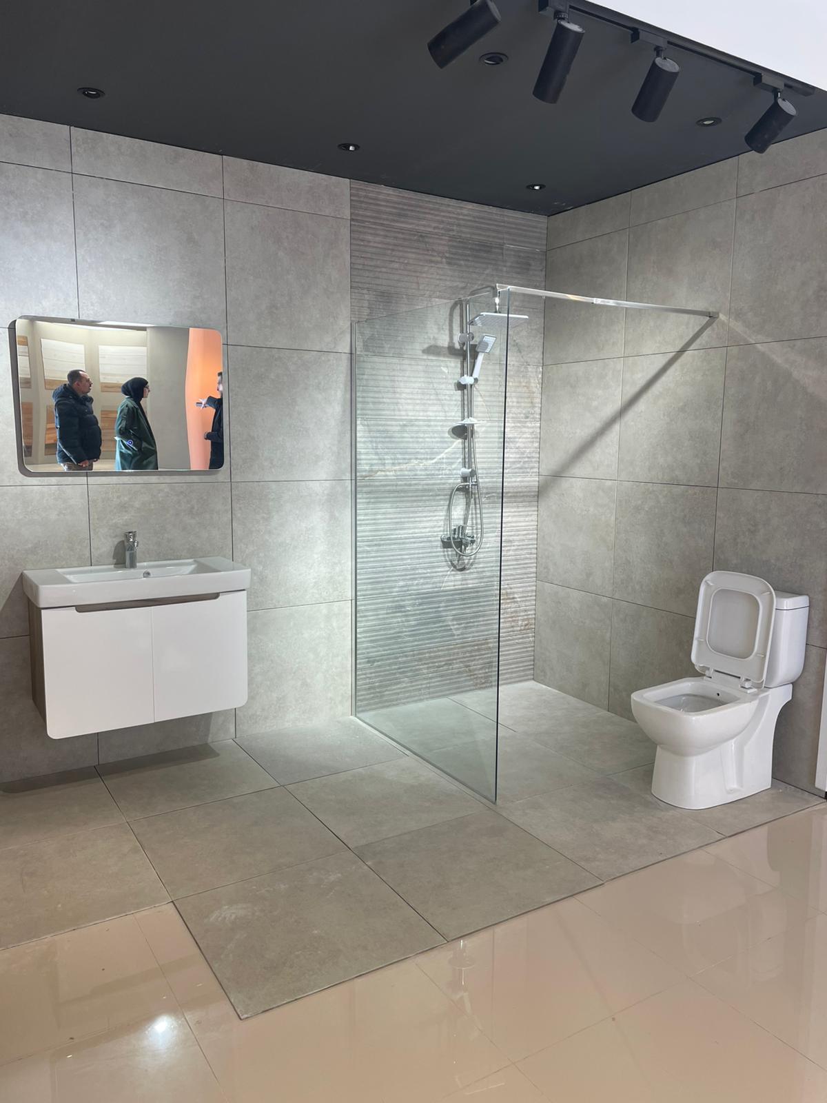 Moderno kupatilo sa elegantnom tuš kabinom od stakla, minimalističkim umivaonikom i savremenim WC-om. Prostor je osvetljen i koristi neutralne tonove za sofisticiran izgled.