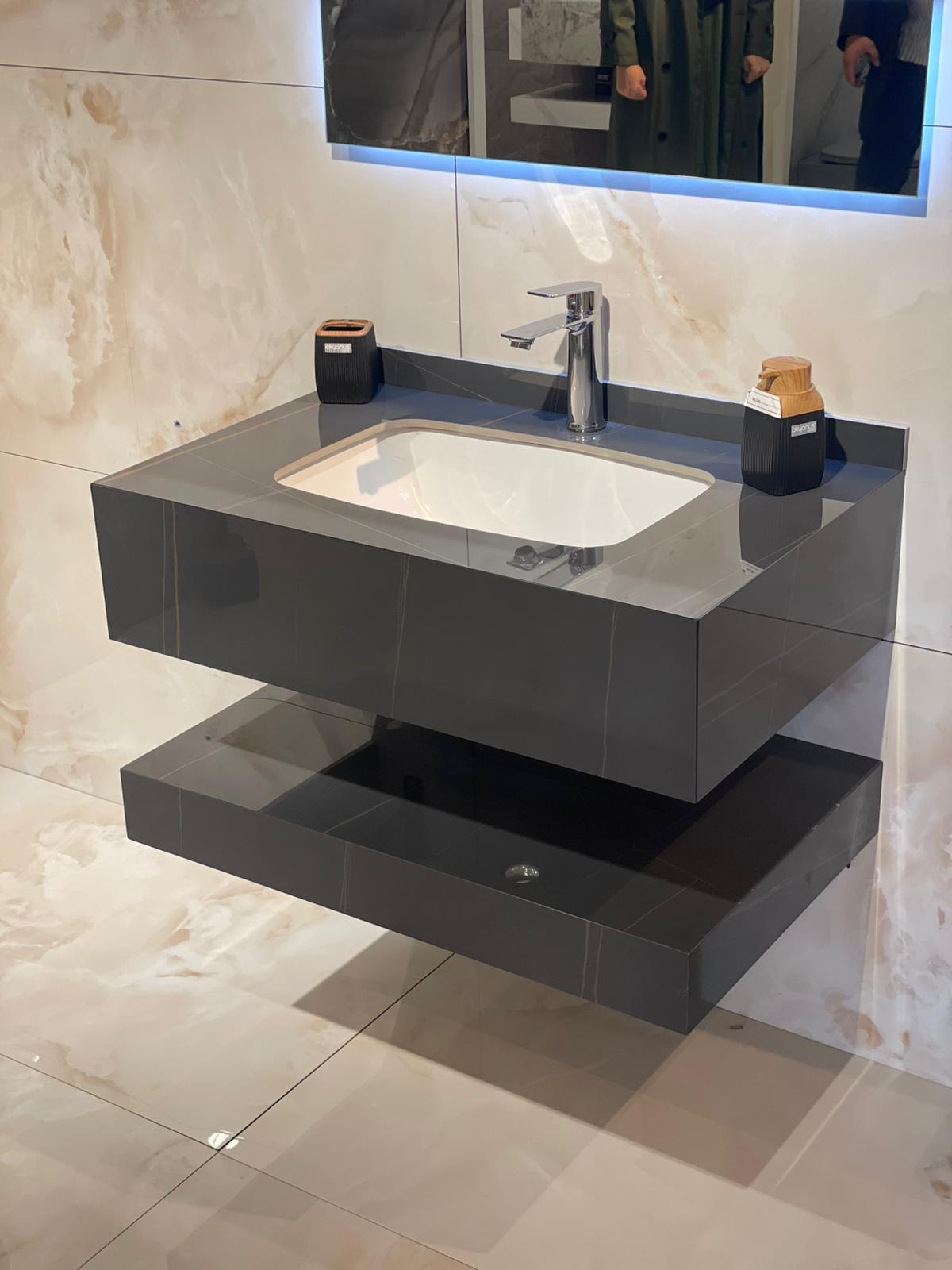 Moderna komoda za lavabo sa minimalističkim dizajnom, izrađena od tamnog materijala sa elegantnim linijama. Uključuje ugradni lavabo i donju policu za odlaganje.