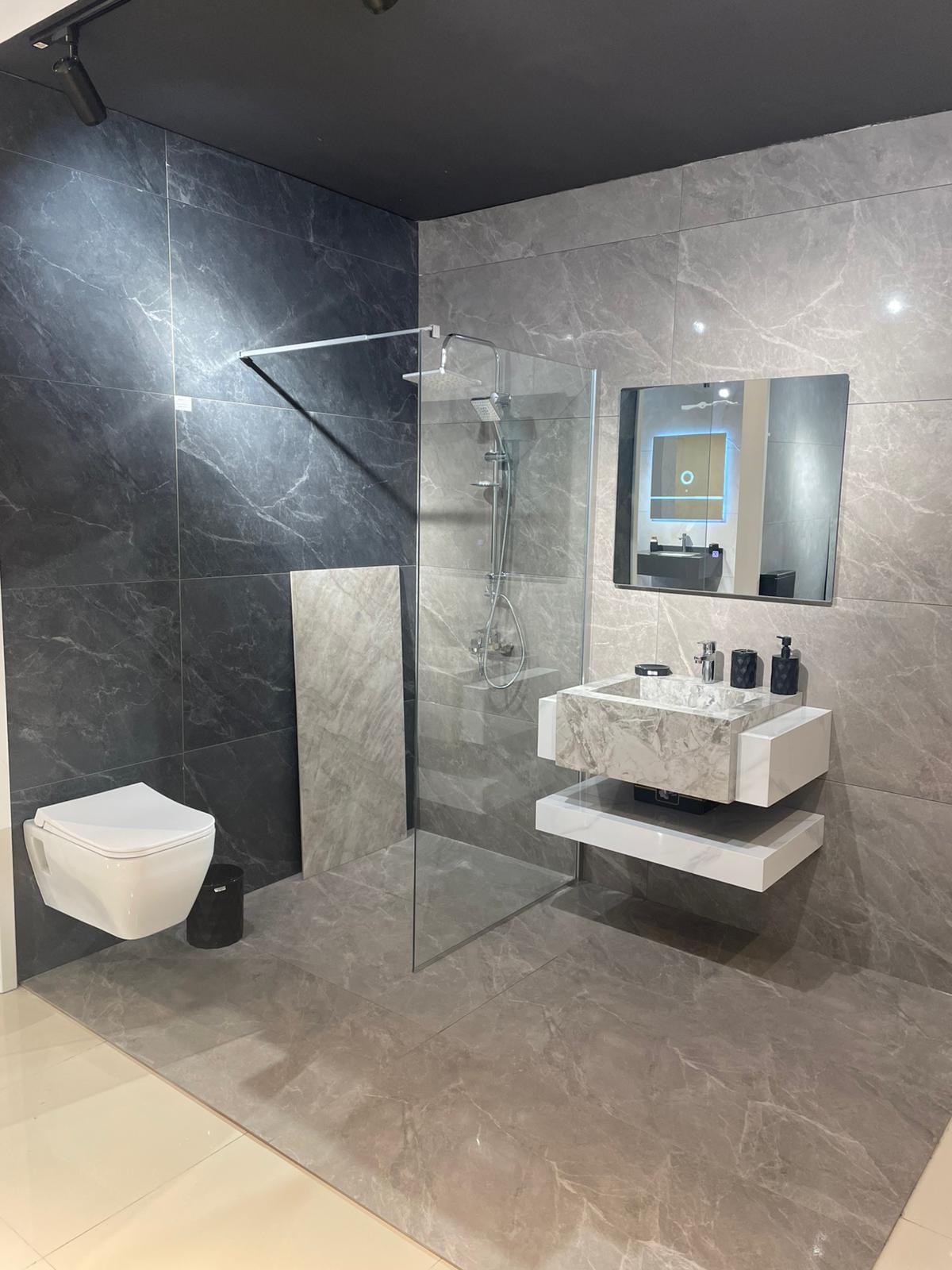 Moderno kupatilo sa elegantnim pločicama u tamnim tonovima. U prostoru se nalazi tuš kabina sa staklenom pregradom, suspendovani WC i minimalistički lavabo sa ogledalom.